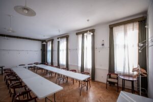 Parkettás terem, a jobb oldali falon ablakokkal. Az ablakos fallal parhuzamosan két sorban hosszú asztalok.