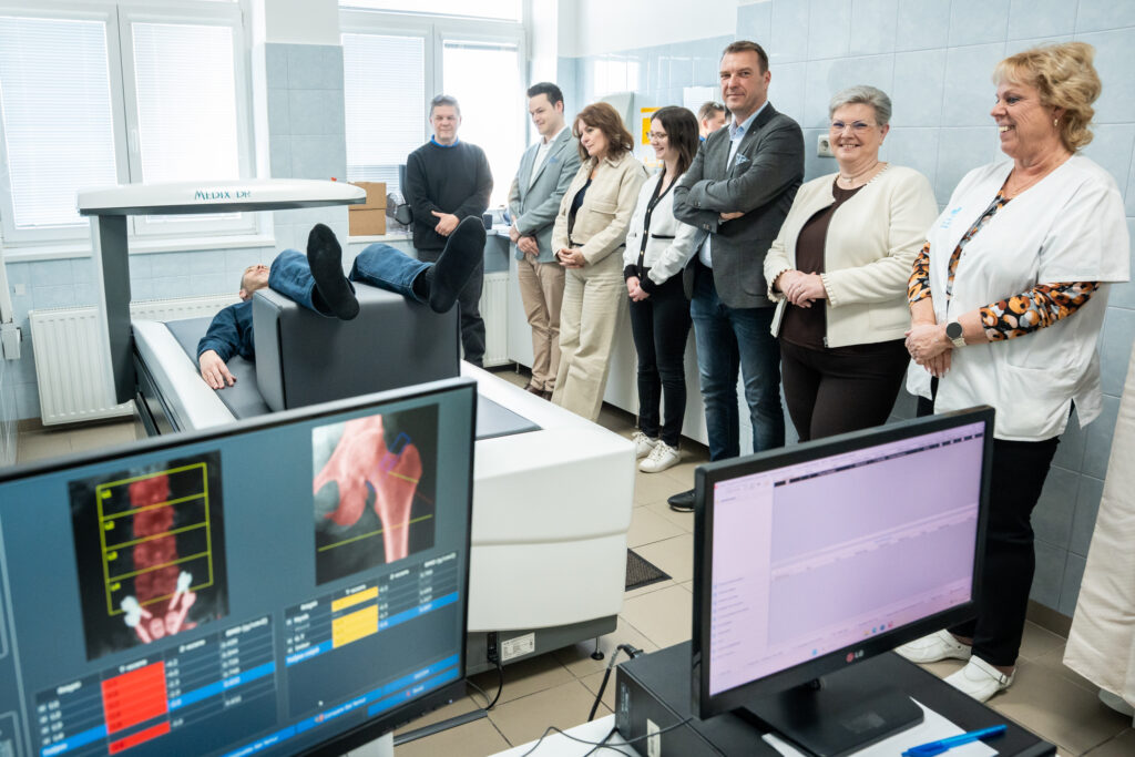 A kerület vezetői megtekintik az új csontsűrűség‑vizsgáló berendezést az egészségügyi intézményben. A képen a modern diagnosztikai készülék és annak működését szemléltető bemutató látható.