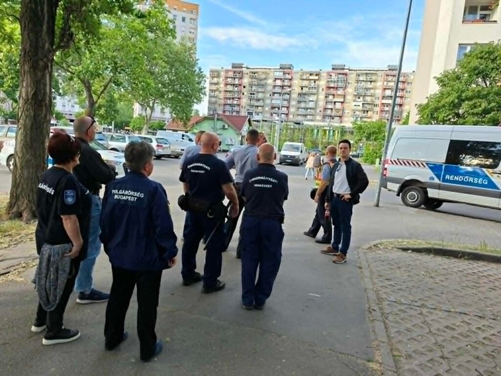 Közbiztonsági járőrszolgálat a XV. kerületben. A képen polgárőrök és rendőrök állnak egy járdaszakaszon, szolgálati járművek mellett, egyeztetés közben.