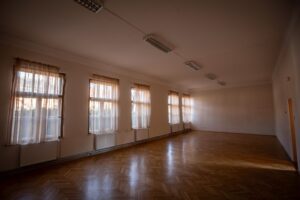Hosszúkás, parkettás terem, baloldalt, az egyik hosszanti oldalon ablakok sora.
