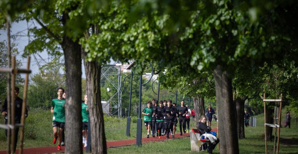 Futókörök Napja a Páskom parkban. A képen sportolók futnak a piros rekortán pályán, körülöttük zöld fák és parkban pihenők láthatók.