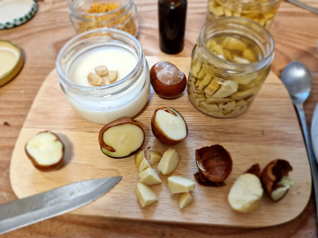 Asztal nagyjából felülnézetben, rajta vágódeszka, üvegek, kés, kanál, gesztenye, van ami még egészben, és van, ami feldarabolva.