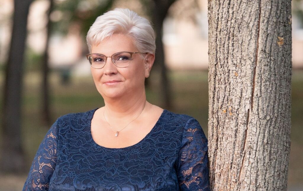 Cserdiné Németh Angéla polgármester egy fánál áll kék ruhában.