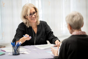 Dr. Fekete Márta geriáter szakorvos demenciaszűrést végez egy résztvevővel a rendezvény helyszínén. Az asztalon vizsgálati lapok és írószerek láthatók