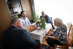 Cserdiné Németh Angéla polgármester, Gyurkó Dániel alpolgármester és Makai Ferenc önkormányzati képviselő beszélget Nagy Jánosné Mészáros Etelkával otthonában, kilencvenedik születésnapja alkalmából. Az asztalon virágcsokor és sütemények láthatók.