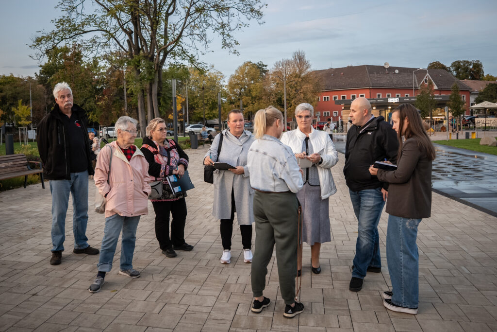 A Palota parkban megrendezett szabadtéri fogadóórán a polgármester egy lakos felvetését hallgatja, miközben jegyzeteket készít. A körülöttük álló érdeklődők és önkormányzati munkatársak a kerületet érintő kérdésekről egyeztetnek a park sétányán.