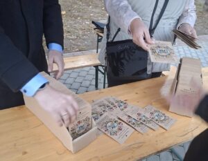 Vadvirágmagokat tartalmazó papírcsomagok egy asztalon a virágmagosztáson. Az előtérben résztvevők veszik át a csomagokat, amelyekből minden kerületi lakos egyet kaphatott.